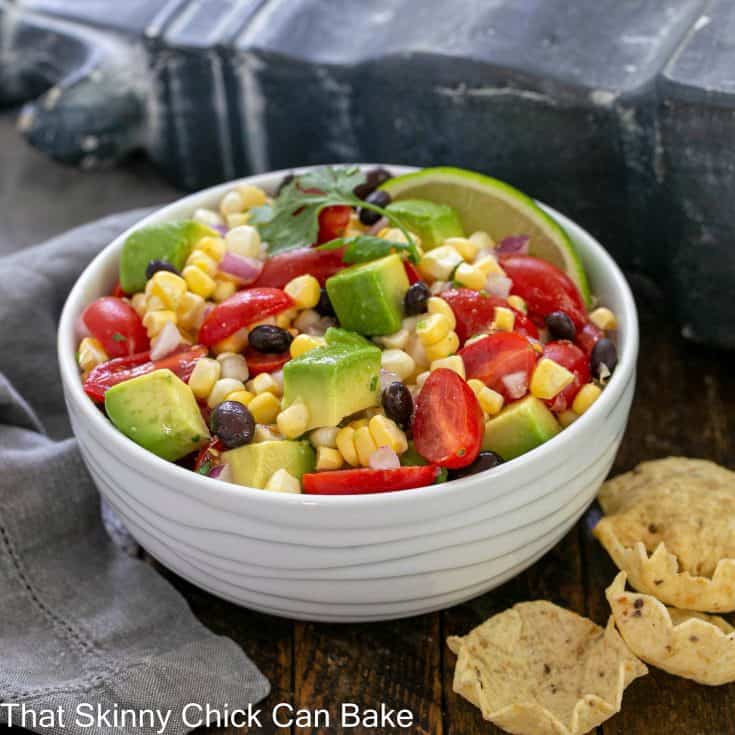 White ceramic serving bowl filled with corn salsa next to a few corn chips