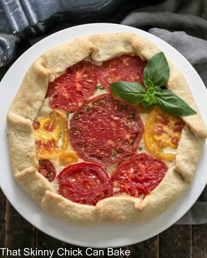 Overhead view of a tomato Galette on a white cake stand with a fresh basil garnish