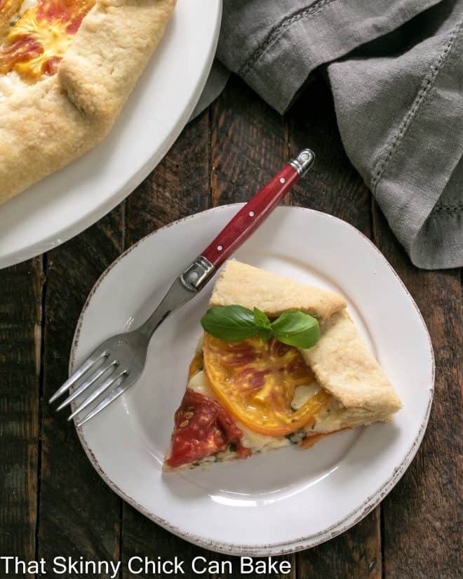 Slice of cheese tomato galette on a white plate with a red fork.