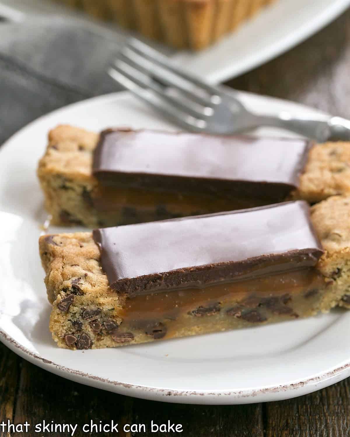 Two slices of chocolate chip cookie tart on a white plate with a fork.
