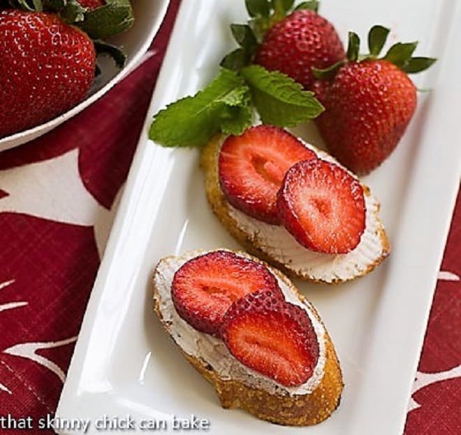 Overhead view of strawberry goat cheese tartines on a white tray garnished with mint and strawberries.