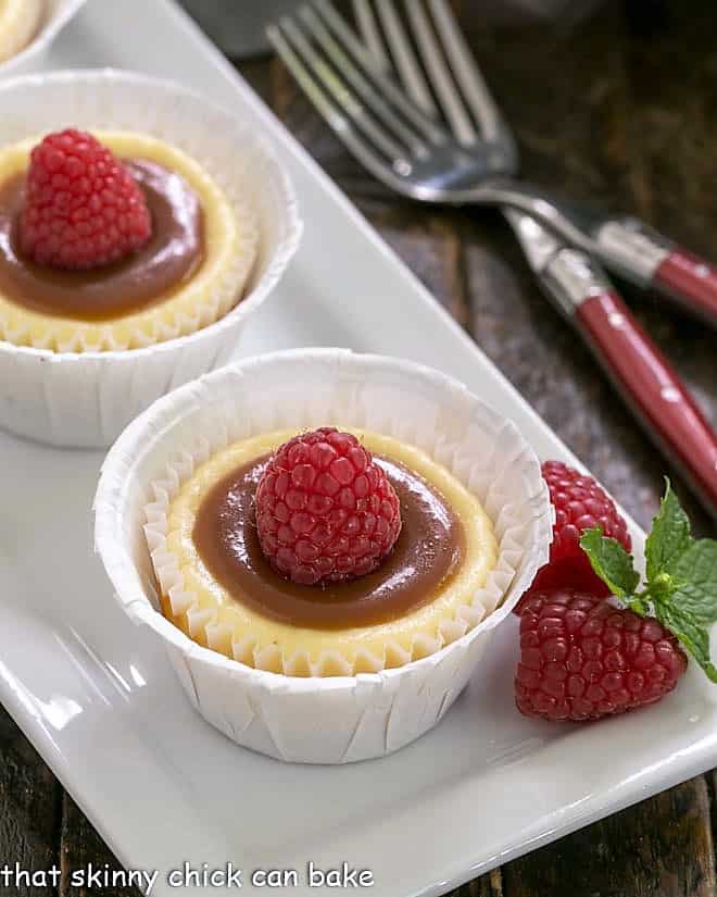 Individual Caramel Cheesecakes - An exquisite combination of flavors and textures in these individual cheesecakes! 2 Caramel Topped Mini Cheesecakes on a white tray.