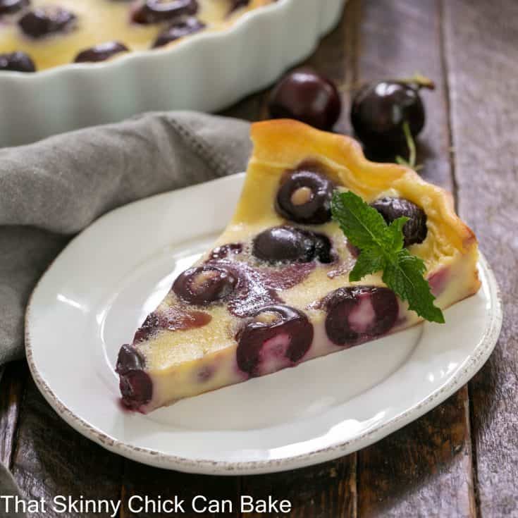 slice of cherry clafoutis on a white plate with a sprig of mint garnish