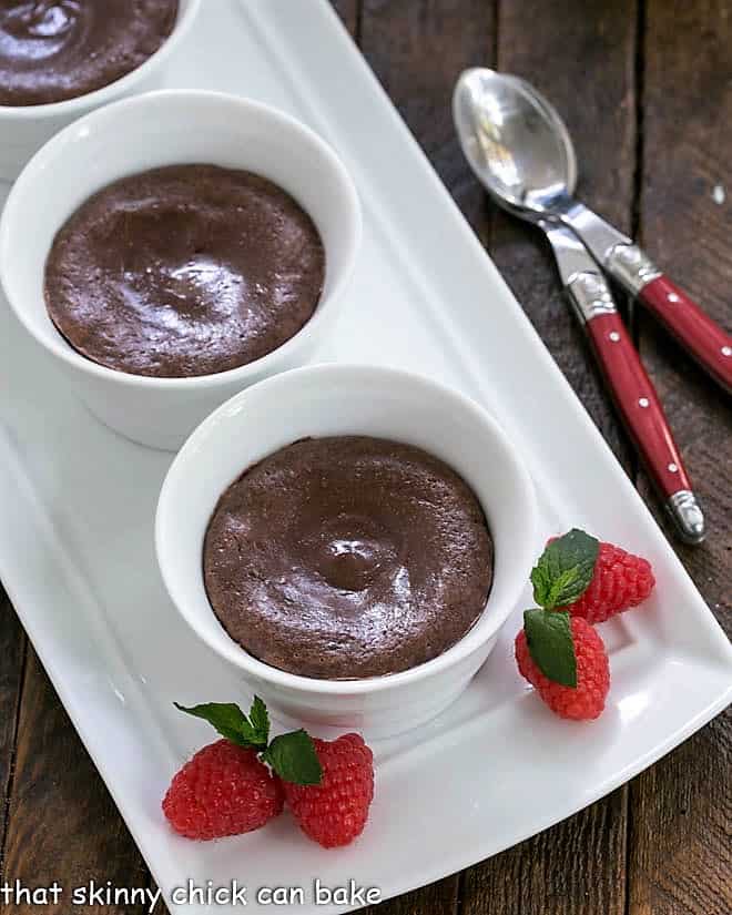 Warm Chocolate Cheesecakes - a rich luscious individual dessert for chocolate and cheesecake lovers alike! 3 warm chocolate cheesecakes on a white tray with raspberries and mint.