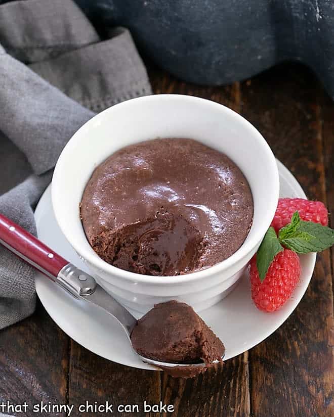 Mini Chocolate Cheesecakes - Individual Warm Chocolate Cheesecakes are perfect for a dinner party! Rich, luscious and perfect for chocolate lovers! Individual chocolate cheesecakes with a spoonful removed onto a red handled spoon.