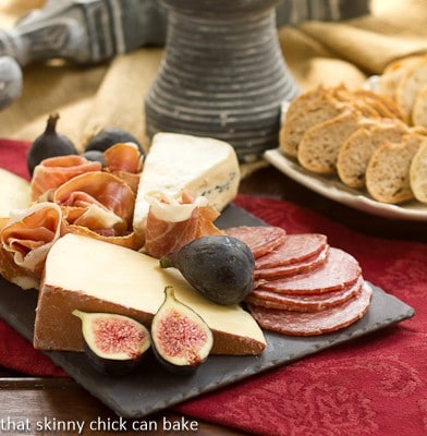 A slate cheese board topped with meat and cheeses on a red napkin.