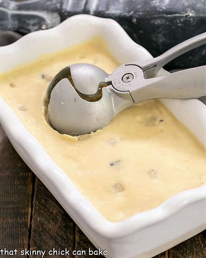 Cookie dough ice cream frozen in a white loaf pan with an ice cream scoop.
