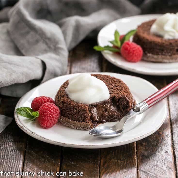 Two lava cakes on white dessert plates with berries, mint and whipped cream to garnish