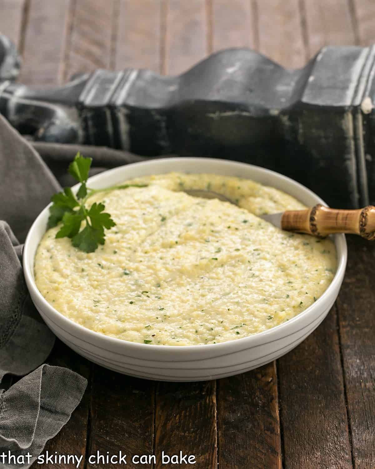 Easy Parmesan Polenta in a white bowl with a bamboo handle spoon garnished with parsley.