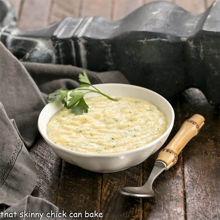 small bowl of polenta garnished with parsley next to a bamboo handle spoon