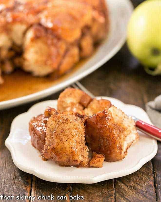 Crock Pot Apple Monkey Bread -- Breakfast dish made easy using canned biscuits and diced apples creating a gooey, cinnamon spiced caramel coating around each delicious bite! Apple Monkey Bread on a small white plate.
