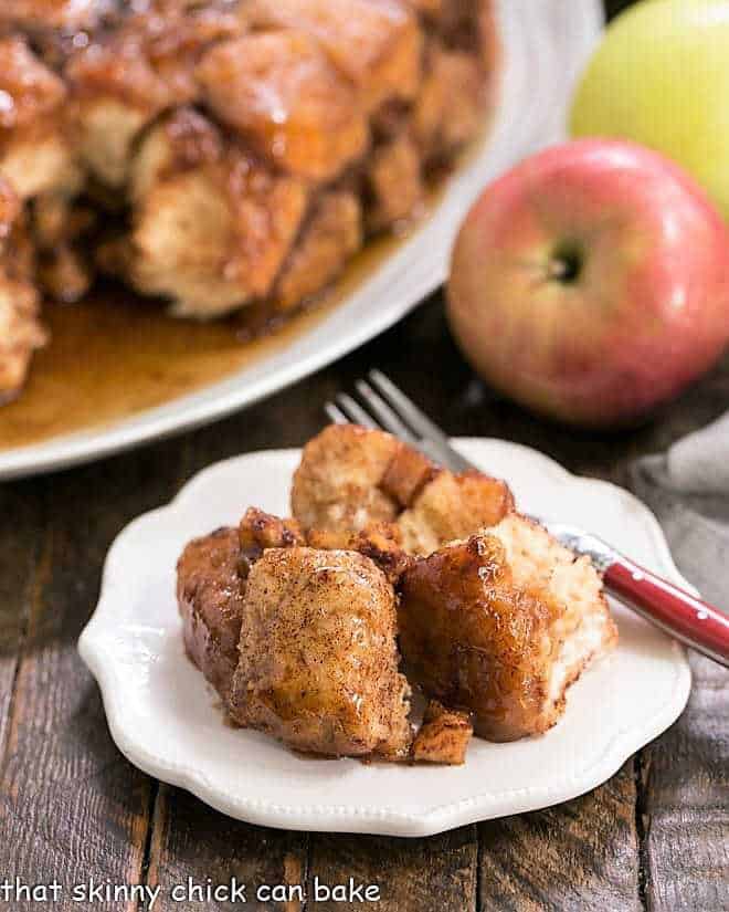 Crock Pot Apple Monkey Bread -- Breakfast dish made easy using canned biscuits and diced apples creating a gooey, cinnamon spiced caramel coating around each delicious bite! Apple Monkey Bread on a white ceramic plate with a red handled fork.