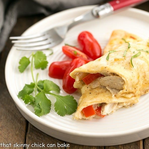 Cheesy Chicken Enchiladas on a white dinner plate with cilantro and grape tomatoes.