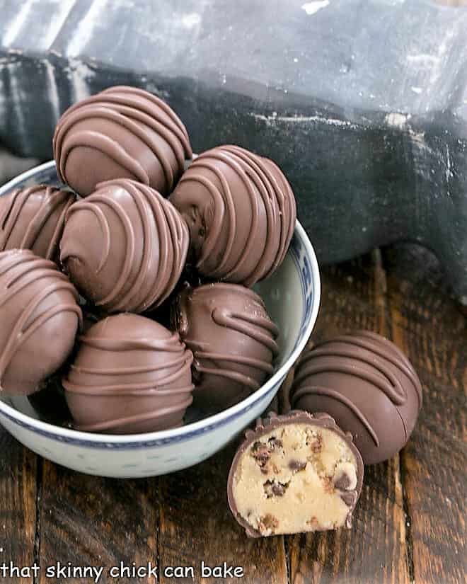 A bowl of cookie dough bites with one whole and one cut open truffle on the side.