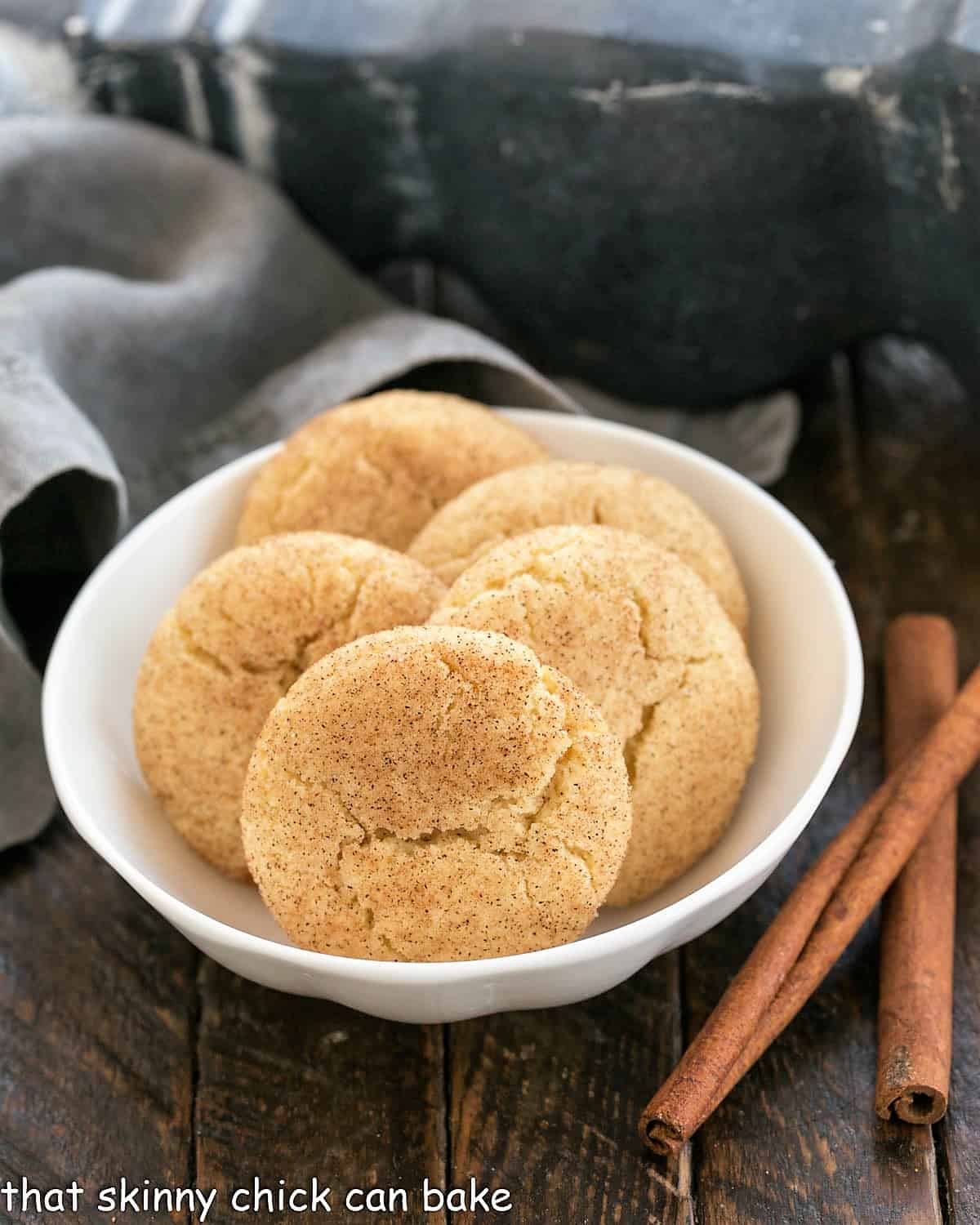 snickerdoodles in a shallow white bowl next to 2 cinnamon sticks