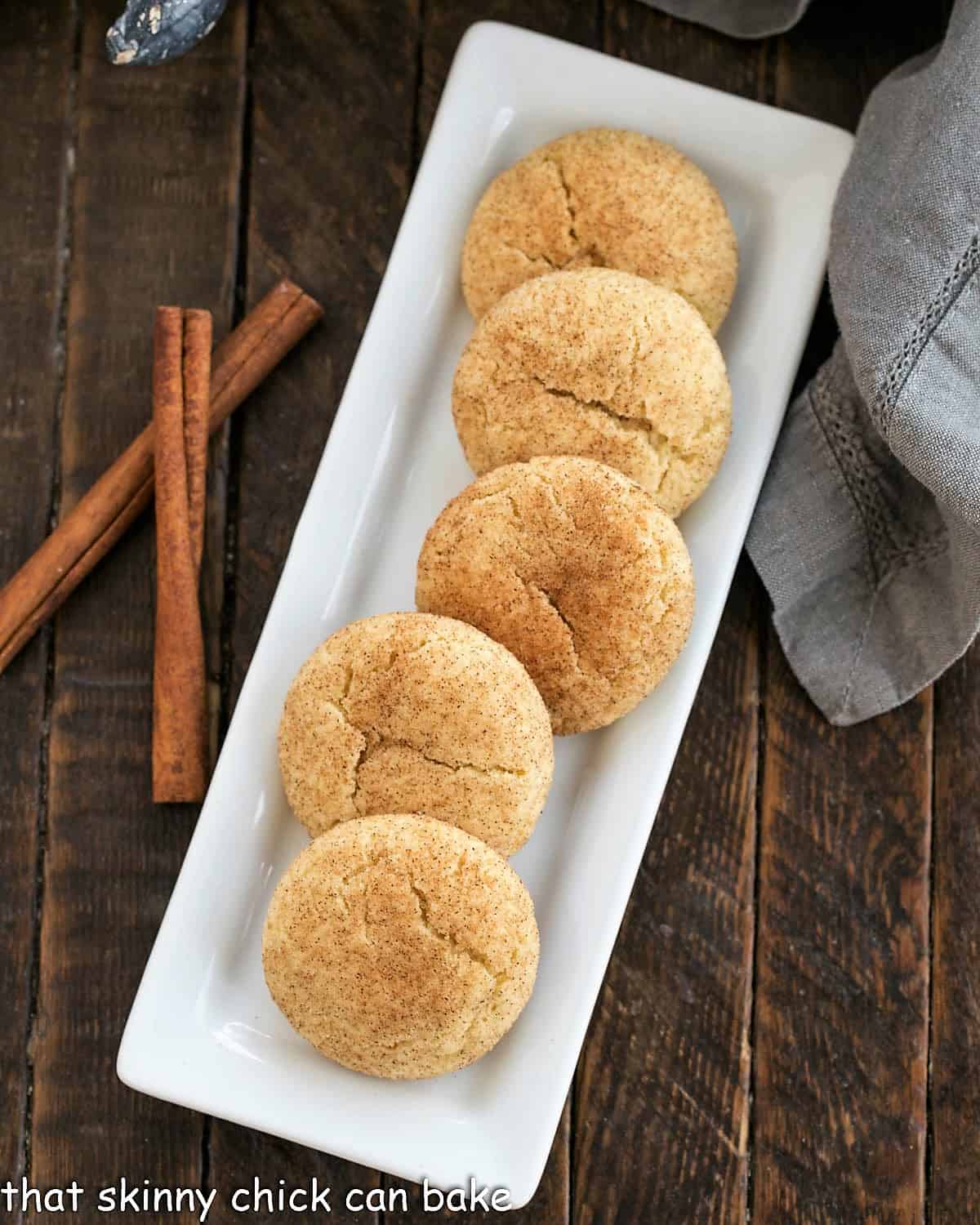 Overhead view of a tray of snickerdoodles next to 2 cinnamon sticks.