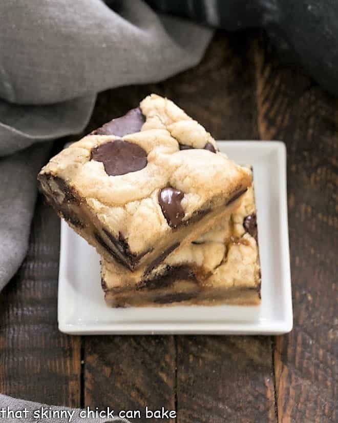 Chocolate Chip Cookie Bars with Caramel - an exquisite combination that's super easy to make! Two caramel chocolat chip bars stacked on a small square white plate.