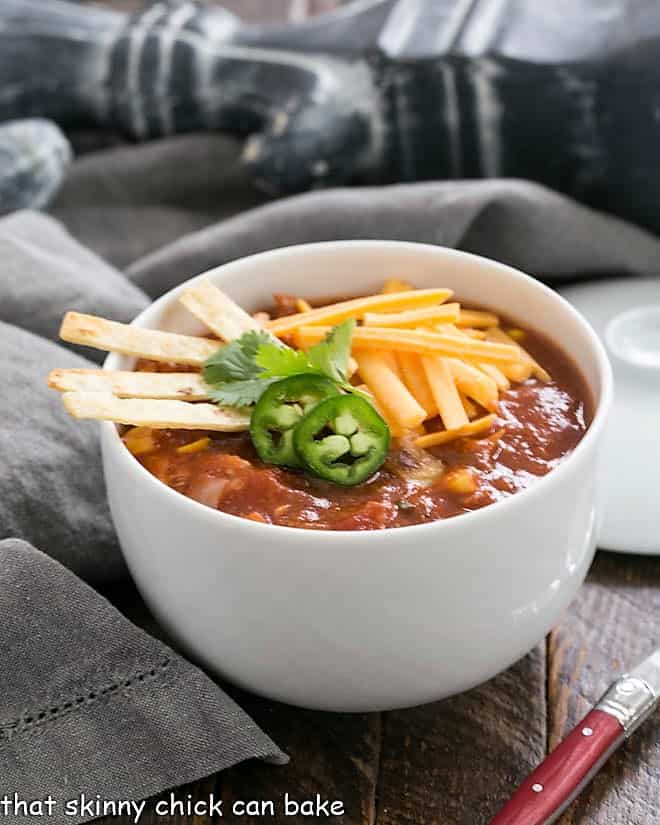 Side view of a white bowl filled with tortilla soup topped with garnishes.