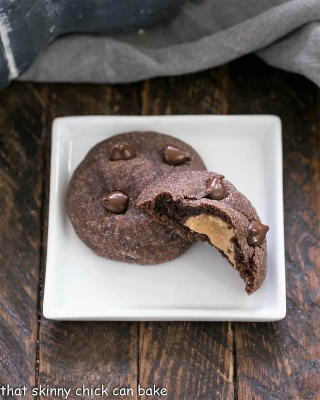 A square white plate with 2 chocolate peanut butter cookies, one broken in half
