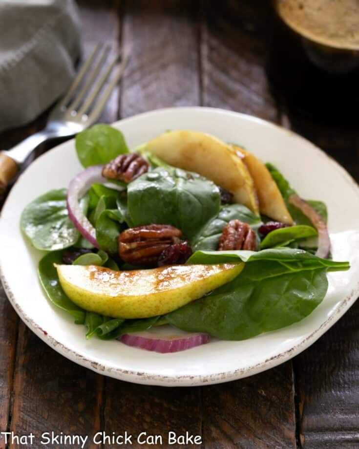 Spianch salad with pears, cranberries and candied pecans on a white salad plate.