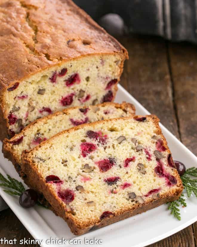 Classic Cranberry Pecan Bread is perfect for the holidays. The sweet-tart, crunchy-crispy components of this cranberry quick bread recipe make this a loaf to remember! Slices of cranberry pecan quick bread on a white tray.