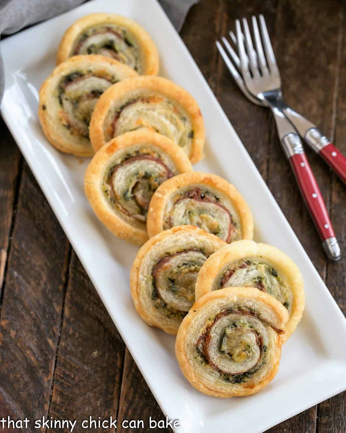 Overhead view of Prosciutto, Gruyere and Basil Pinwheels on a rectangular white ceramic tray.