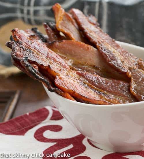Candied Bacon AKA Pig Candy - a sweet salty treat that's a terrific option for breakfast or for a fun appetizer! Candied Bacon AKA Pig Candy in a white bowl viewed from the side.