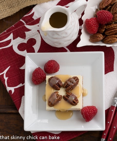 Overhead view of Caramel Pecan Cheesecake Bars on a square white plate garnished with raspberries.