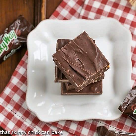 Milky Way Fudge squares stacked on a white plate over a red and white checked napkin.