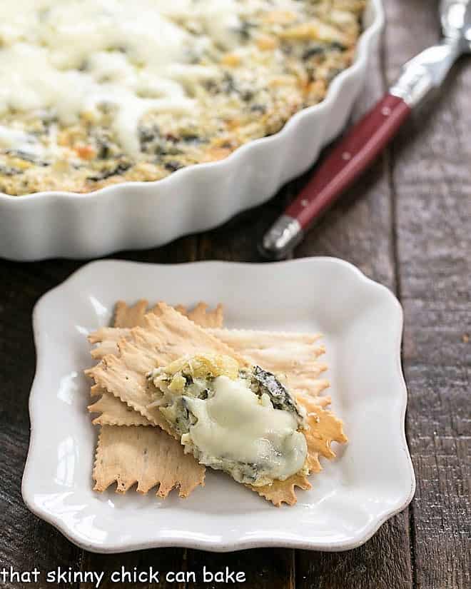 Spinach Artichoke Dip - A perennial party favorite A spoonful of Hot Spinach and Artichoke Dip on an appetizer plate with crackers.