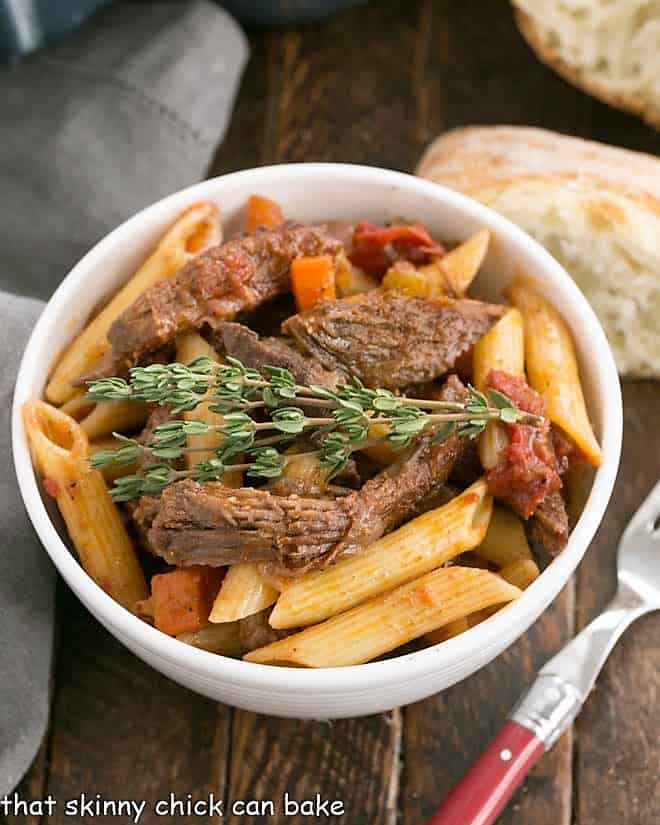 Beef Ragu with penne pasta - a twist on the classic boeuf bourguignon in a pasta dish! Beef Ragu with penne pasta in a white bowl with bread slice and a fork.
