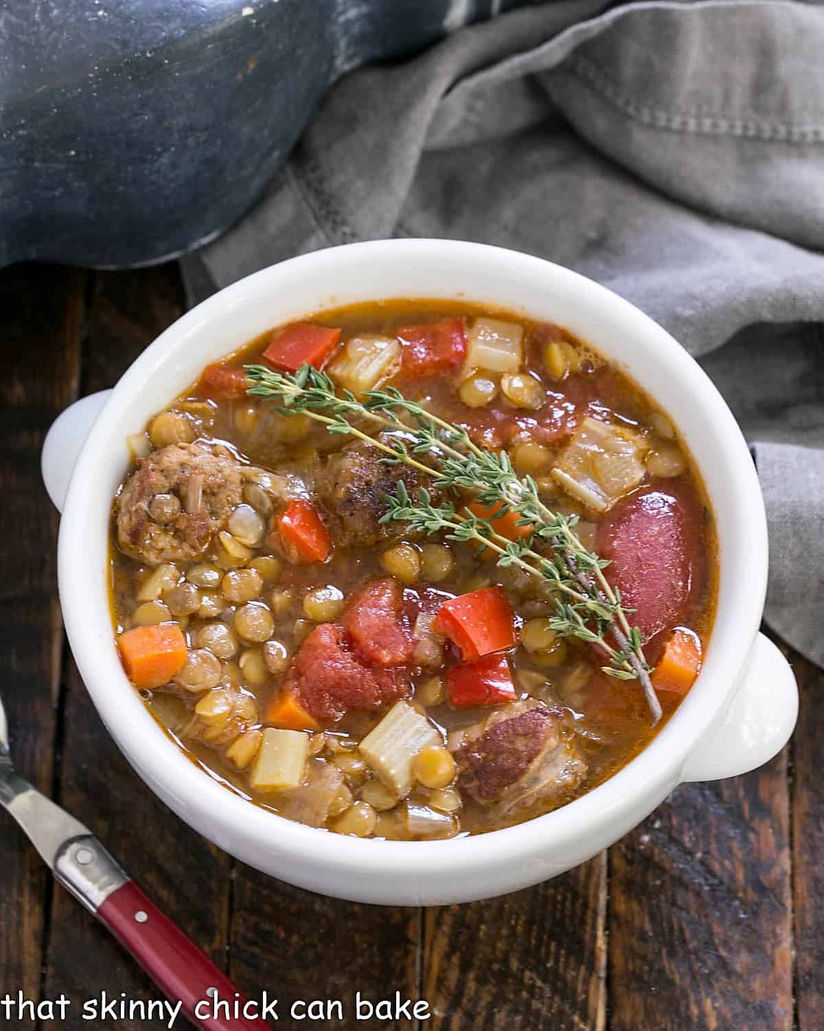 Overhead view of sausage lentil soup in a white bowl garnished with fresh thyme.
