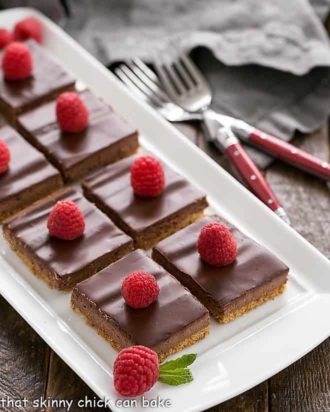 Dark Chocolate Mousse Bars - a delicious layered bar cookie with a graham cracker crust, mousse filling and ganache topping! Dark Chocolate Dessert Bars on a white tray garnished with raspberries and mint