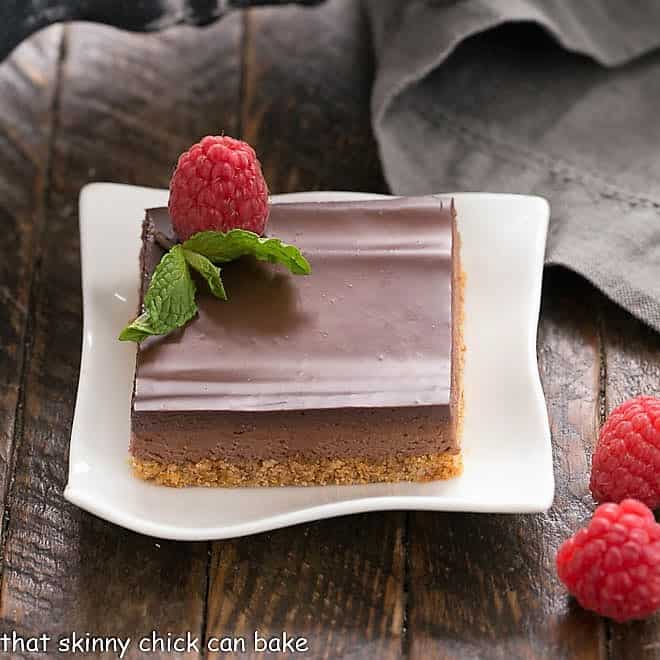 Dark Chocolate Mousse Bars - a delicious layered bar cookie with a graham cracker crust, mousse filling and ganache topping! A slice of Dark Chocolate Mousse Bars on a white plate topped with a raspberry