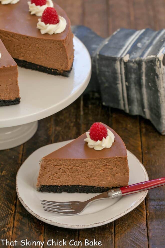 Slice of Italian Cheesecake on a white plate in front of the remaining cheesecake on a cake stand.
