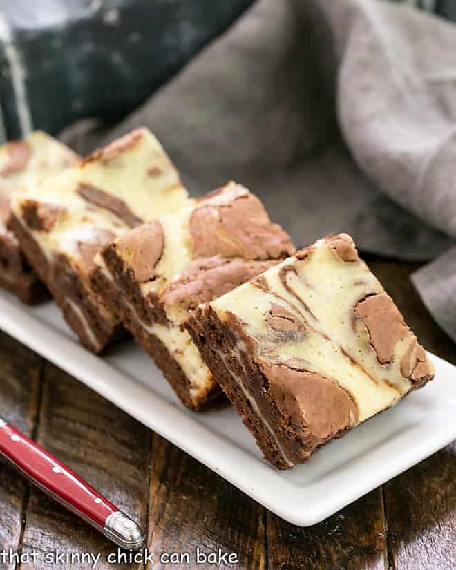 Cheesecake Swirl Brownies lined up on a white ceramic tray with a red handle fork.