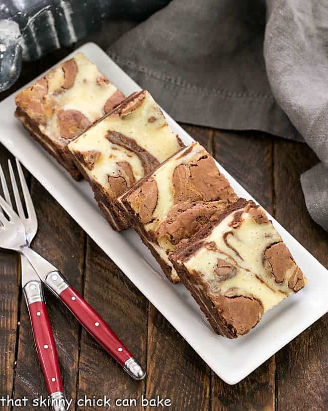 Overhead view of a tray of cheesecake brownies with two red handled forks.
