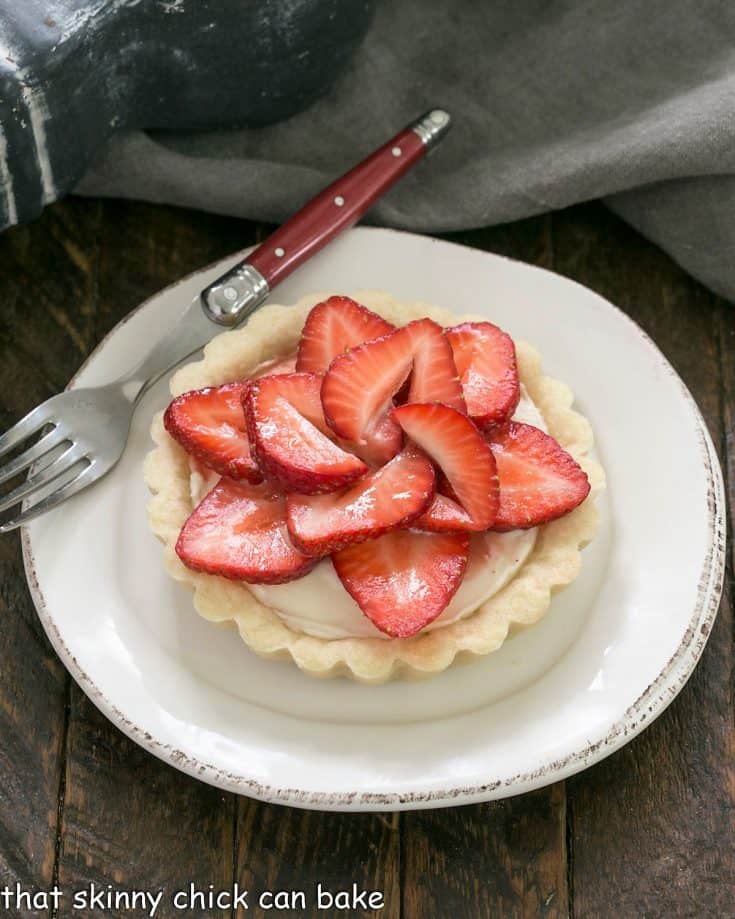 A strawberry fruit tart on a round white dessert plate with a red handle fork