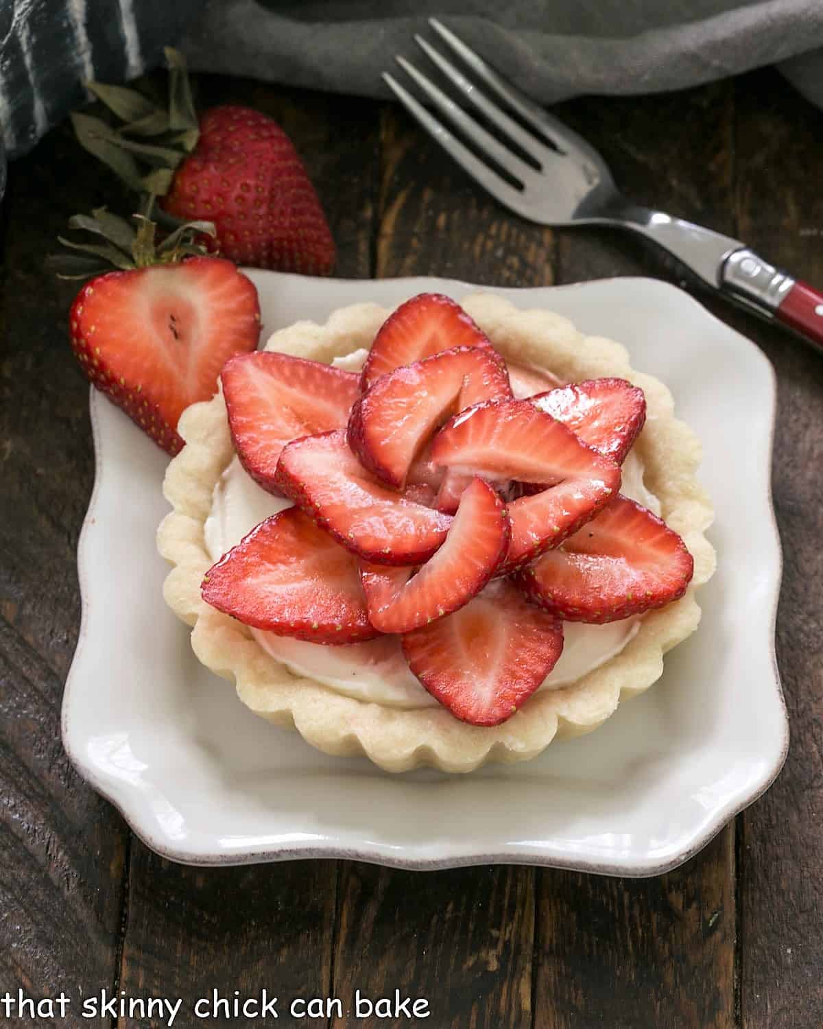A strawberry tart on a square white plate with a red handled fork.