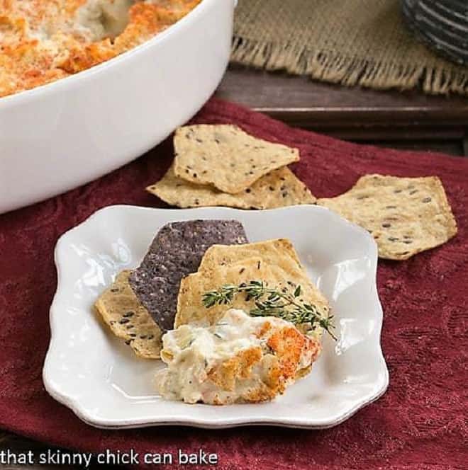 Hot Artichoke Shrimp Dip on a square white plate with chips and a sprig of thyme.
