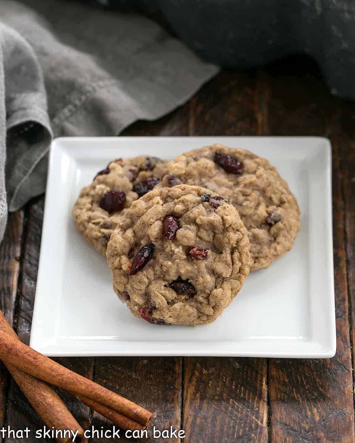3 Oatmeal Craisin Cookies on a square white plate next to 2 cinnamon sticks.