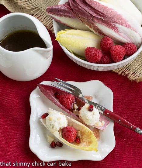 Endive Cups with Blue Cheese, Raspberries and Macadamia Nuts on a square white plate with a drizzle of vinaigrette.