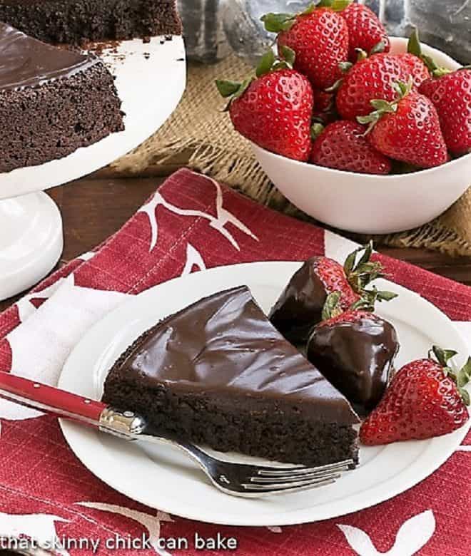 Flourless Double Chocolate Cake slice on a white plate with chocolate covered strawberries.