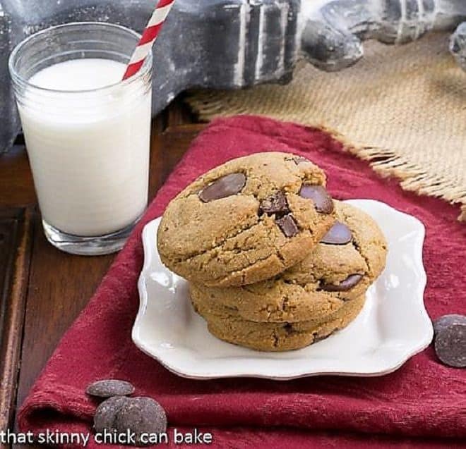 Jumbo Chocolate Chips stacked on a white square plate with a glass of milk.