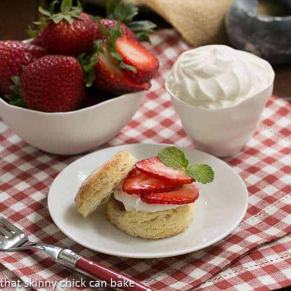 Double strawberry rose shortcake on a white plate next to bowls of strawberries and cream.