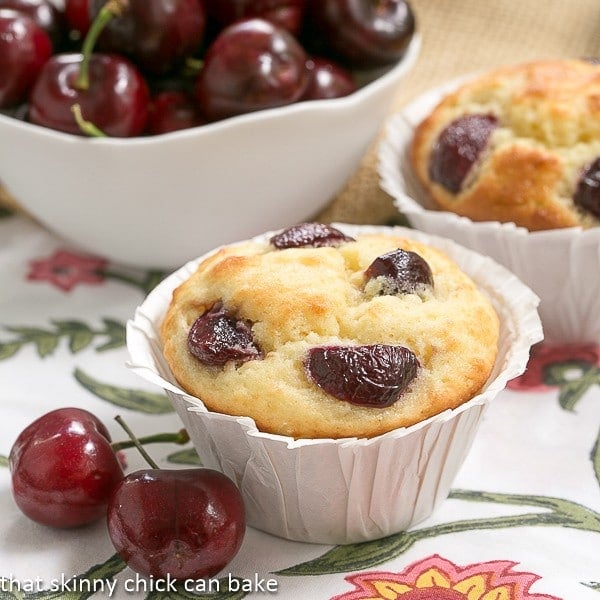 Double Cherry Muffins - Scrumptious, tender muffins with two kinds of cherries! A wonderful cherry recipe! Double Cherry Muffins close up view with fresh cherries in a white bowl on a floral napkin