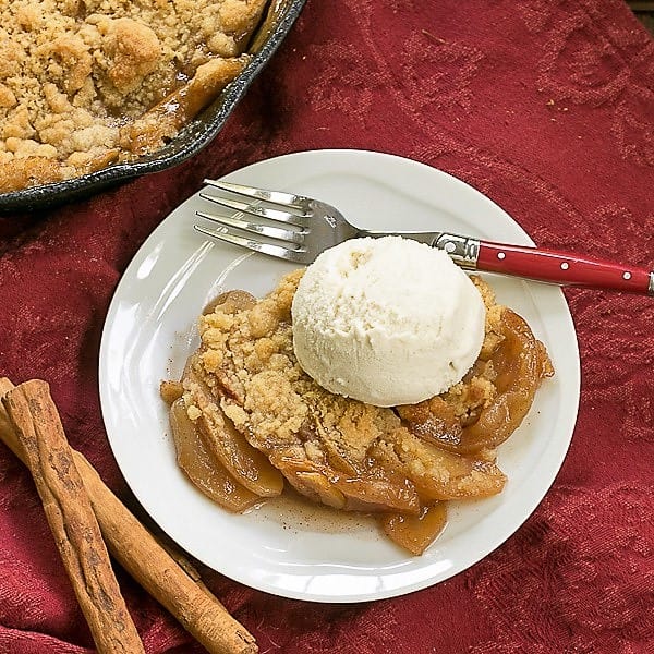 Grilled Apple Crisp - A classic dessert with smoky undertones from the BBQ Overhead view of Grilled Apple Crisp on a round white plate with a scoop of vanilla ice cream.