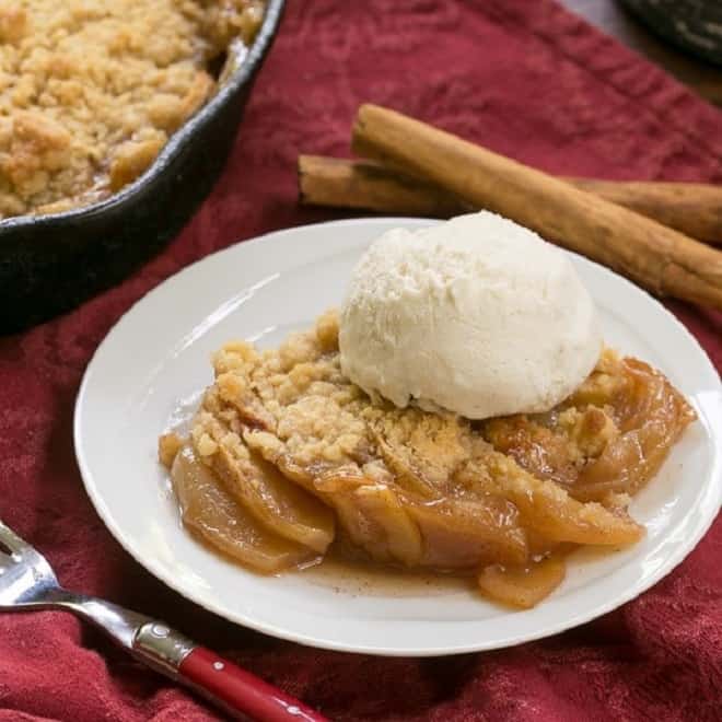 Grilled Apple Crisp - A classic dessert with smoky undertones from the BBQ Grilled Apple Crisp topped with vanilla ice cream with a red fork and cinnamon sticks.