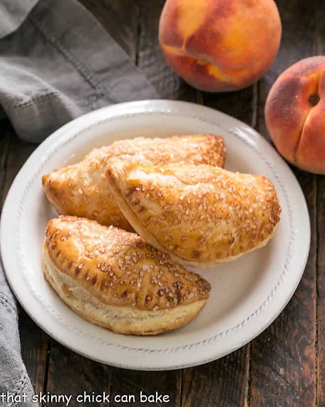 Chaussons aux Pêches or Peach Turnovers - scrumptious, homemade peach hand pies Overhead view of 3 peach turnovers on a white plate.