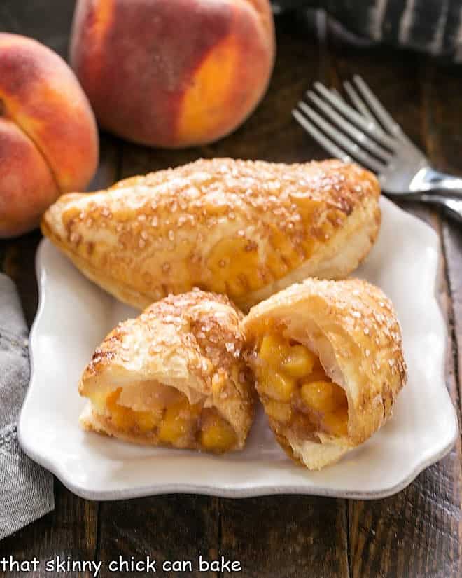 Chaussons aux Pêches or Peach Hand Pies - scrumptious, homemade peach turnovers Chaussons aux Pêches with one broken in half showing the peach filling on a white ceramic plate.